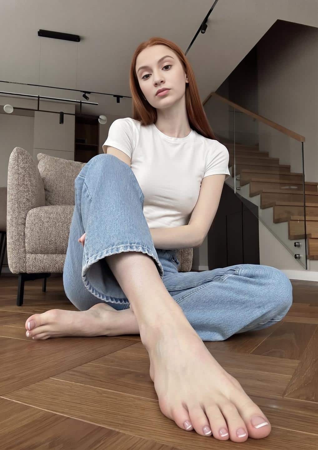 AI-generated sexy indoor floor pose with one bare foot, long toes, and neutral toe nail polish close to the camera